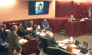 In this image taken from video, Tom Sullivan, right, gives testimony, as picture is displayed on the wall of his late son Alex, who was killed by Colorado theater shooter James Holmes, who sits fifth from left in a dark shirt, during Holmes' trial, in Centennial, Colo., Tuesday, Aug. 4, 2015. Alex Sullivan went to the movie theater to celebrate his 27th birthday and his first wedding anniversary, his father testified. (Colorado Judicial Department via AP, Pool)